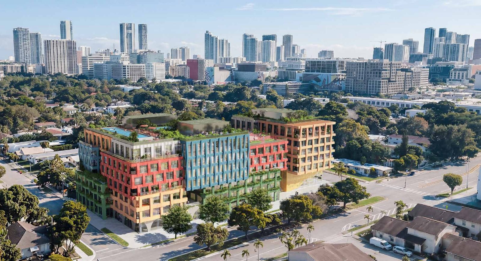Rendu aérien du projet d’immeuble WOMA à Wynwood Norte, avec sa façade tissée rouge, bleue et verte et le downtown de Miami en arrière-plan